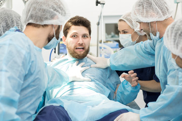 Group of surgeons holding scared male patient on surgery table