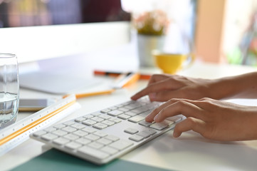 Cropped shot female hands using computer, typing on keyboard.