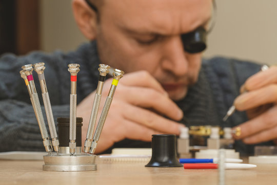 Mature watchmaker repairing mechanical watch at his workshop - Powered by Adobe