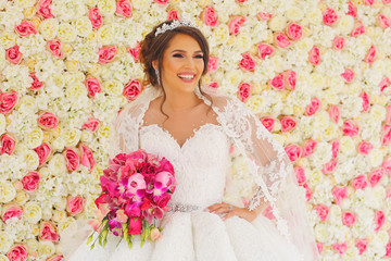 Obraz na płótnie Canvas Beautiful fashion bride posing with bouquet of flowers in front of wedding flower wall