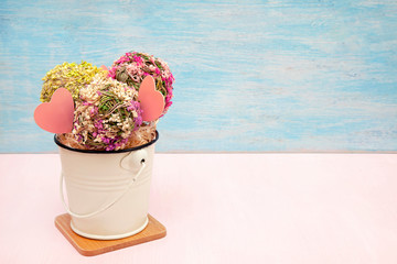 Decorative flower balls in a white bowl on a wooden stand Light pastel color background. Copy space for your text.