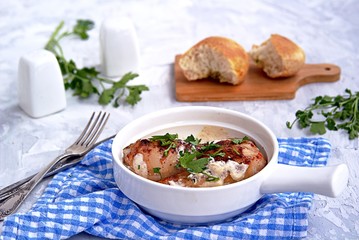 Fried chicken in a creamy garlic sauce or chkmerili chicken in a portioned ceramic pan on a light gray background. Georgian cuisine. Selective focus.