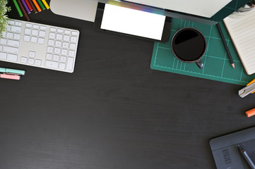 Creative desk workspace with mockup tablet computer and office equipment on black table, top view.
