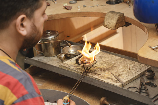 Mature jeweler welding gold while restoring jewelry at his shop