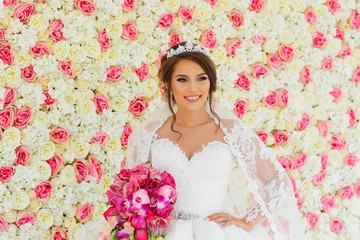 Beautiful fashion bride posing with bouquet of flowers in front of wedding flower wall