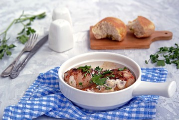 Fried chicken in a creamy garlic sauce or chkmerili chicken in a portioned ceramic pan on a light gray background. Georgian cuisine. Selective focus.