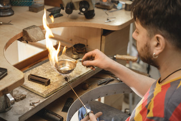 Mature jeweler welding gold while restoring jewelry at his shop