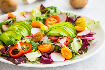 Healthy salad with fresh vegetables, avocado, tomatoes, pepper, radishes, green arugula, onion, spinach and lettuce with olive oil