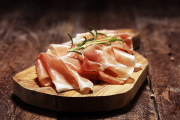 Italian prosciutto crudo or jamon with rosemary. Raw ham on rustic background
