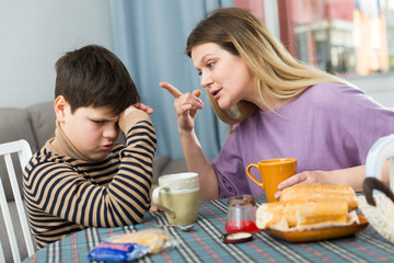 Upset mother and  unhappy son arguing during breakfast indoors