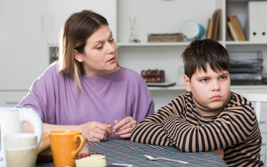 Upset boy and angry mother having quarrel during breakfast at home