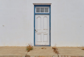 Minimalist capture of a single rural door on a white textured wall.  Door has blue frame in a state...