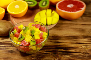 Tasty fruit salad in glass bowl and fresh fruits on the wooden table