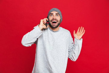 Fototapeta premium Image of successful man laughing while using cell phone isolated over red background