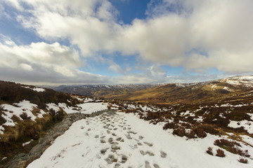 A snowy mountain path under a majestic blue sky and white clouds