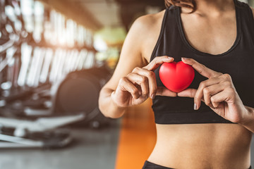 Happy sport woman holding red heart in fitness gym club. Medical cardio heart strength training lifestyle. Pretty female sport girl workout exercise. Cardiac healthy and well-being. Massage ball in ha
