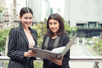 Two young Asian businesswomen looking into document file folder for analyzing profit or sale break even point after marketing. Business teamwork employees of lifestyle working women concept.