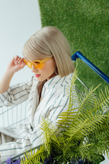 beautiful stylish blonde girl in sunglasses and fashion clothes posing on green grass