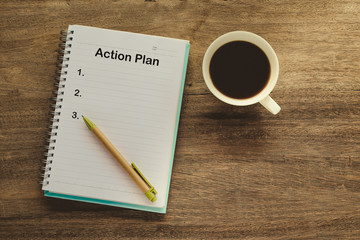 Action Plan text on book note with cup of coffee, pen.