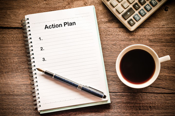 Action Plan text on book note with cup of coffee, pen.