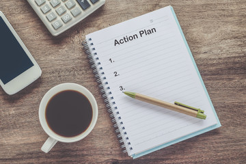 Action Plan text on book note with cup of coffee, pen.