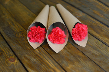 Three red carnations in Kraft paper on wooden background. Congratulations on the victory day on may...