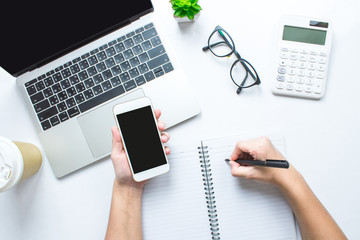 Businessmen use laptops and smartphones and write notes on the notebook at the desk.