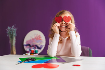 Cute little girl making a heart from paper