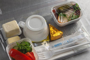 Food served on board of economy class airplane. Plastic lunchbox with food and disposable tableware.