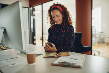 Smiling businesswoman reading a text message at her office desk