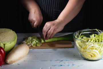 Female Chef cutting leek on wooden table, hands, close up.  Menu, recipe book. Diet healthy food. Selective focus.