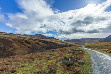 A mountain view with grassy slope, rocky summits and path under a majestic blue sky and white clouds
