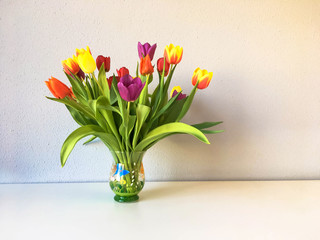 Colorful bouquet of tulips stands in a vase on the table.
