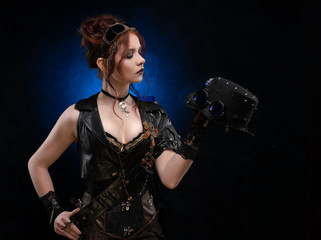 Beautiful redhead cosplayer girl wearing a Victorian-style steampunk corset and leather vest, with large breasts in a deep neckline and glasses holding a hat on dark blue background