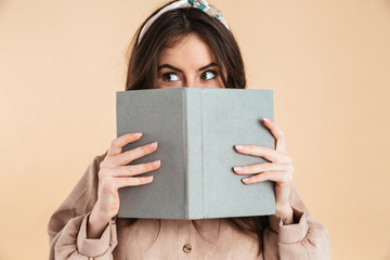 Young pretty woman posing isolated over beige background wall holding book reading.