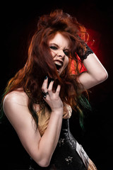 Beautiful redhead cosplayer girl wearing Victorian-style steampunk dress screams and shooks her hair with her hands. Red and black background.