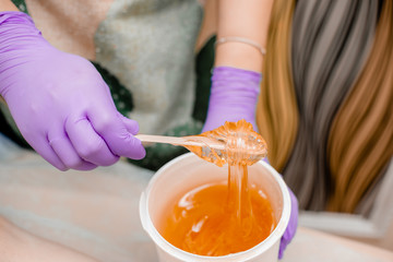 Wax bar with sugar paste depilation and beauty concept - sugar paste or wax honey for hair removing with bright  purple gloves hands of cosmetologist in spa salon. Top view several objects