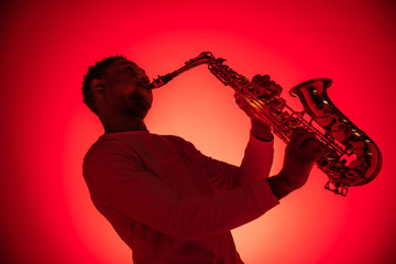 Fototapeta na wymiar African American handsome jazz musician playing the saxophone in the studio on a neon background. Music concept. Young joyful attractive guy improvising. Close-up retro portrait.