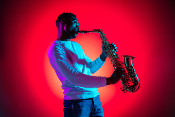 African American handsome jazz musician playing the saxophone in the studio on a neon background....