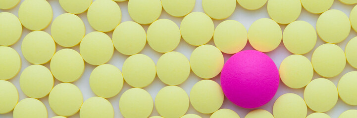 Small yellow and one pink pills on a white background close-up.