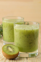 Fototapeta na wymiar Kiwi smoothies in a glass next to fresh kiwi slices on a natural wooden table.