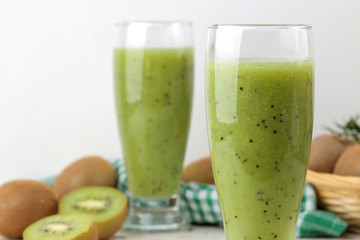 Kiwi smoothies in a glass next to fresh kiwi slices on a light marble table. fruit drink.