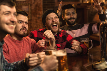 Young happy men watching football game on TV at the pub drinking beer