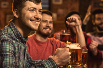 Young happy men watching football game on TV at the pub drinking beer
