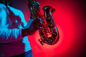 African American handsome jazz musician playing the saxophone in the studio on a neon background. Music concept. Young joyful attractive guy improvising. Close-up retro portrait. - obrazy, fototapety, plakaty