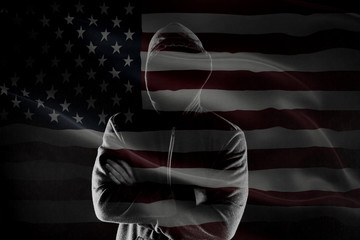 Double exposure of concept of criminal in USA with silhouette of male with crossed hands in hood and flag
