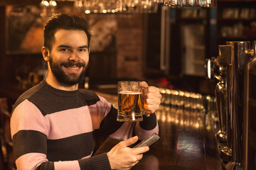 Young man using his smart phone while drinking beer