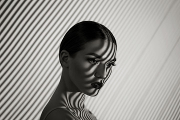 Black and white portrait of a beautiful young girl with a shadow pattern on the face and body in the form of stripes.