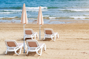 Umbrellas and chaise lounges on the beach. Empty plastic sunbeds near the sea. Tropical vacation,...