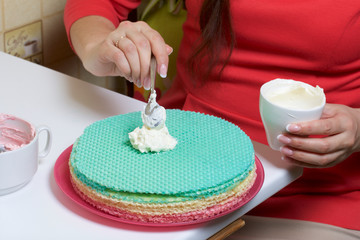 A woman lubricates the cakes and puts in a pile. Round wafer cakes of different colors. For making waffle cake. Nearby there is a can of condensed milk to soak the cakes.